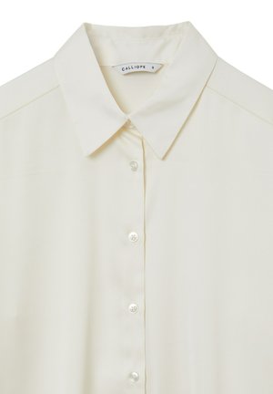 Chemise col mao beige clair avec une texture lisse, fermeture à boutons et un léger éclat. L'étiquette indique "CALLIOPE", taille S.