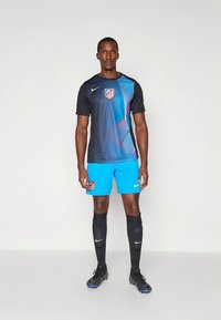 Musta ja sininen raidallinen urheilupaita, jossa on joukkueen logo, yhdistettynä kirkkaan sinisiin shortseihin ja mustiin sukkiin, suunniteltu urheilusuorituksiin.