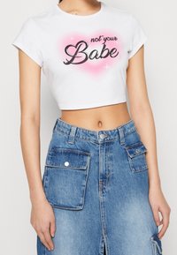 Vit croppad t-shirt med texten "not your Babe" i svart och en rosa hjärtbakgrund, parat med en blå denimkjol med fickor och en slits.