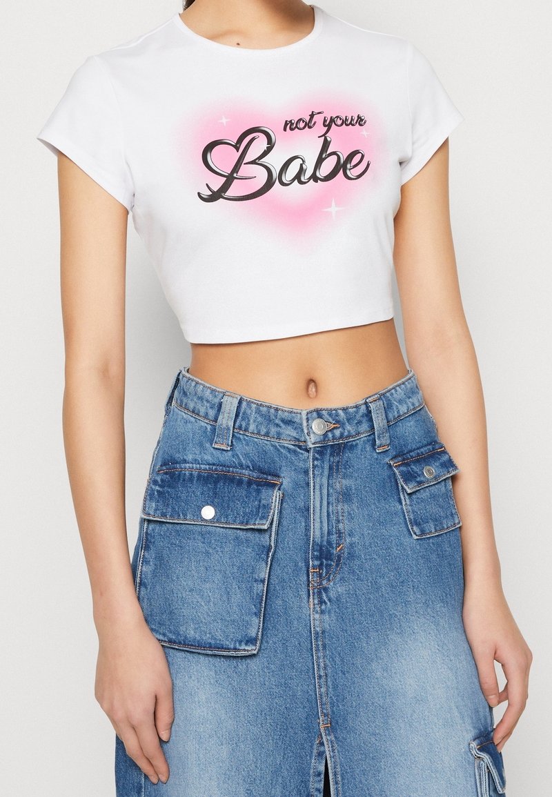 Vit croppad t-shirt med texten "not your Babe" i svart och en rosa hjärtbakgrund, parat med en blå denimkjol med fickor och en slits.