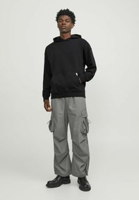 Black hoodie with a kangaroo pocket, paired with light gray cargo pants featuring side pockets and elastic cuffs, worn with black boots.