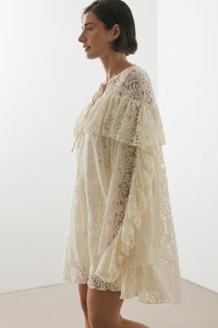 Kermanvärinen pitsimekko, jossa on röyhelökaulus ja -hihat, löysä malli ja monimutkainen kukkakuosi, teksturoitu kangas.