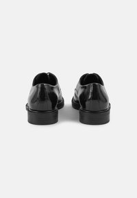 Scarpe in pelle nere con superficie liscia, punta rotonda e tacco basso, dotate di un dettaglio a cucitura e design slip-on sul retro.