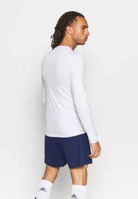Langärmliges, weißes Sportshirt mit glatter Textur, kombiniert mit dunkelblauen Shorts und weißen Socken, das ein einfaches Design und eine gute Passform zeigt.
