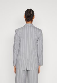 Szara marynarka w prążki o dopasowanym kroju, z klapami wciętymi, pojedynczym rozcięciem z tyłu i długimi rękawami. Materiał wydaje się być gładką tkaniną.