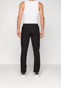 Sorte bukser med lige pasform, prydet med baglommer, båret med en hvid tanktop og hvide sneakers. Glat stofstruktur.