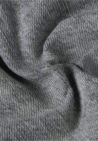 Harmaa kangas, jossa on herringbone-kuvio, esittelee pehmeän, teksturoituneen pinnan. Käärittynä näyttämään monimutkaisia kudontakuviota ja varjojen vaihteluita.