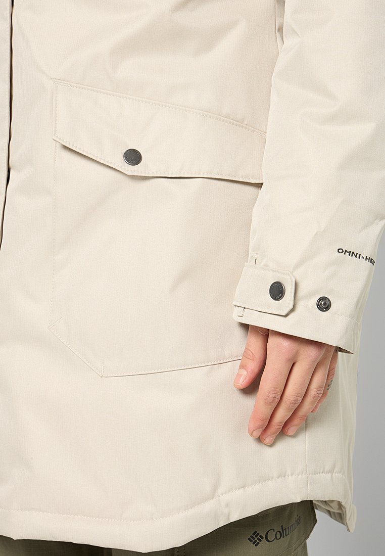 Beige Winterjacke mit Ärmel, Druckknopf-Carrier und verstellbarem Bündchen, teilweise sichtbare Hand, "OMNI-HEAT"-Text auf dem Bündchen.