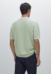 Polo a maniche corte di colore verde chiaro, tessuto texturizzato, colletto classico, polsini e orlo inferiore a costine. Indossato con jeans blu scuro.