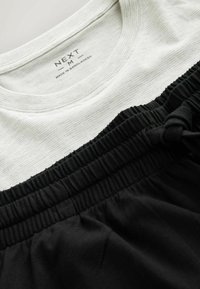 Gros plan d'un t-shirt gris clair col rond avec une étiquette taille M et un pantalon noir à taille élastique avec cordon.