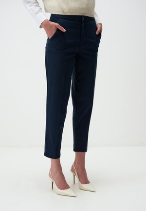 Pantalons taillés navy en coton, présentant une coupe slim, des poches latérales et des ourlets retroussés, associés à des chaussures à talons hauts crème.