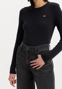 Czarna bluzka z długim rękawem o dopasowanym kroju, z małym czerwonym logo Levi's, połączona z wysokim stanem szarymi dżinsami.