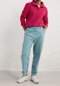 Rosa texturerad tröja med krage och två knappar, ihopparad med ljusblå avsmalnande byxor med sidofickor, upprullade muddar och neutrala sneakers.