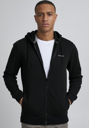 Black zip-up hoodie made from cotton blend. Features front pockets, a drawstring hood, and logo detail on the chest. Smooth texture.