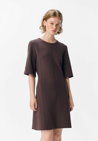Brun klänning med korta ärmar, med rund halsringning och vertikala sömdetaljer, tillverkad av textil med struktur och form.