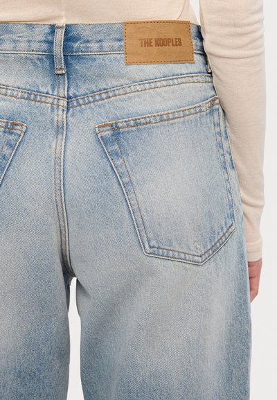 Light blue denim jeans with a faded finish, featuring two back pockets, a leather patch reading "THE KOOPLES," and contrast stitching.