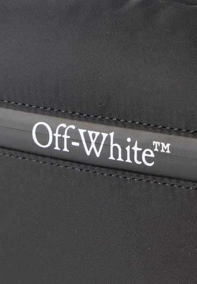 Κοντινή λήψη μαύρου υφάσματος με ραμμένη ραφή και λευκό λογότυπο "Off-White™" τυπωμένο σε μαύρη λωρίδα.