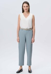 Biała bezrękawnikowa bluzka z dekoltem w kształcie litery V, zestawiona z jasnoniebieskimi spodniami i plecionym paskiem. Czarne buty wsuwane dopełniają całość.