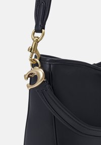 Czarna skórzana torebka o zaokrąglonym kształcie, z złotym zapięciem i metalowymi akcentami. Pasek ma gładką teksturę i jest przymocowany do korpusu.