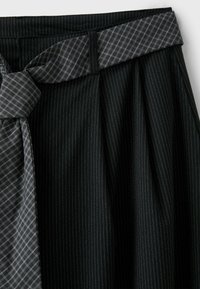 Jupe noire à fines rayures avec une ceinture en tissu écossais gris contrastant nouée en nœud à la taille.