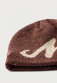Ciemnobrązowa czapka dziergana z kremowym abstrakcyjnym wzorem. Teksturowany wełniany materiał z kolorowymi plamkami. Na dole zagięty mankiet.