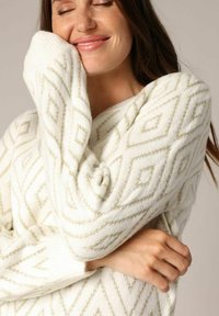 Pull blanc avec un motif de diamants texturé en fils dorés. Tissu doux avec des manches longues, coupe légèrement oversize.