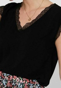 Černý top s V-dekolté, zdobený krajkovým lemem kolem dekoltu a rukávů, doplněný sukní s květinovým vzorem.