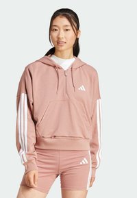 Roza kapuca s puloverjem s sprednjim žepom, bele črte ob rokavih in belim logotipom na prsih. Usklajeno z roza kratkimi hlačami.