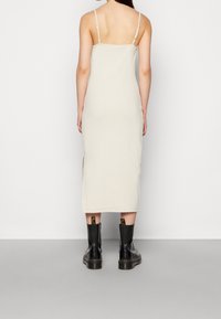 Světle béžové midi šaty s tenkými ramínky, hladkou texturou a bočními rozparky. Kombinované s černými kotníkovými botami s silnou podrážkou.