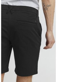 Black shorts made of cotton blend with a smooth texture, featuring a back pocket, a loop drawstring, and a subtle logo detail.