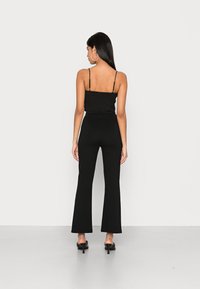 Top preto com corpete franzido e alças finas, combinado com calças flare pretas de cintura alta e sapatos de salto aberto pretos.