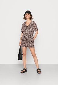 Macacão de estampa de leopardo rosa com mangas curtas e decote em V, combinado com sandálias pretas e uma bolsa preta. Design simples, ajuste confortável.