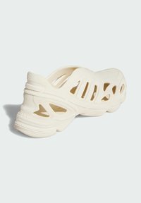 Ivory slip-on shoe with a textured pattern, open mesh design, and rounded shape. Features cutouts for breathability and a flexible sole.