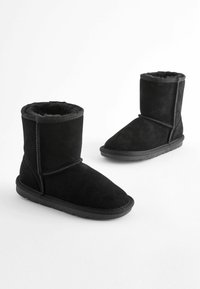 Schwarze Ankle Boots aus Wildleder mit einem weichen, fellgefütterten Innenleben. Mit einer abgerundeten Zehenpartie und einer flachen Gummisohle. Genähte Details entlang der Nähte.