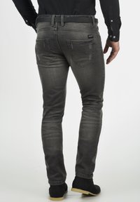 Vaqueros de denim gris ajustados con un acabado deslavado, que cuentan con dos bolsillos traseros y detalles de costura sutiles, combinados con calzado negro.