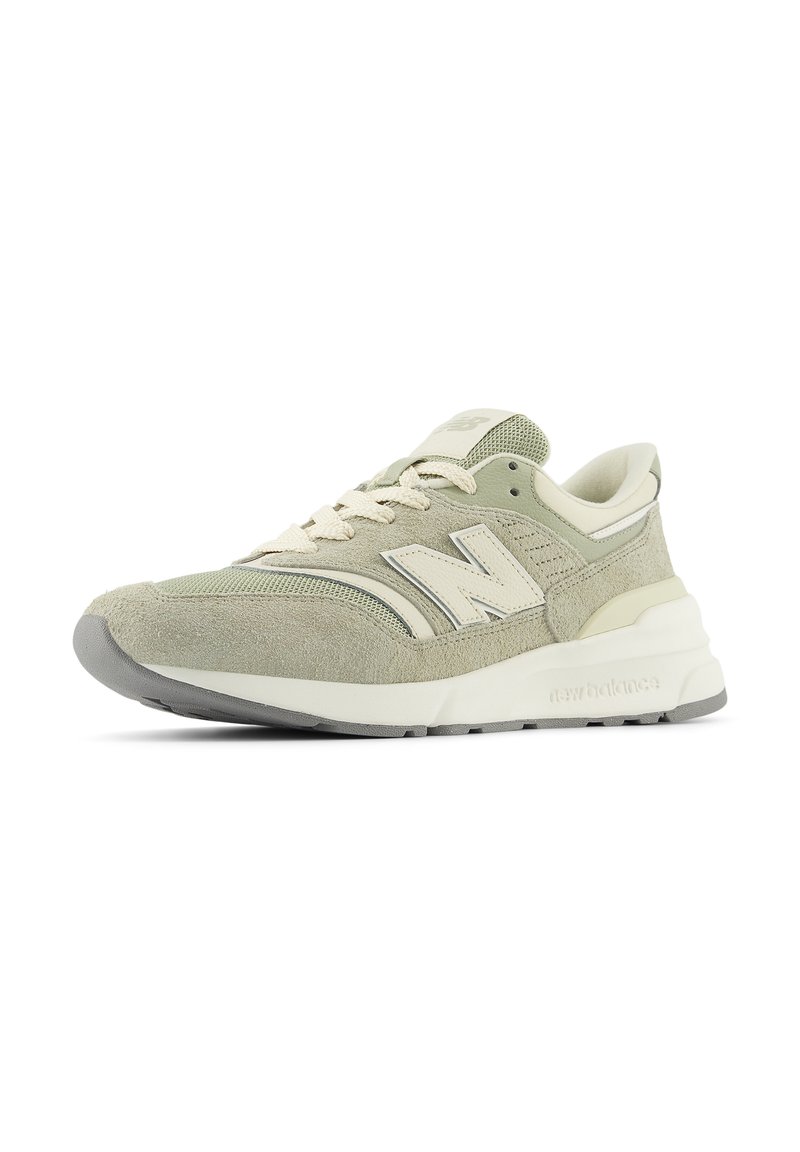 Sneaker New Balance di colore beige chiaro e grigio con tomaia in suede e mesh, design con lacci e suola spessa bianca, mostrata da un angolo laterale.