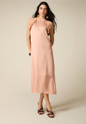 Donna con i capelli lunghi e scuri che indossa un vestito midi rosa cipria senza maniche, con collo a halter e dettagli arricciati, abbinato a sandali neri con tacco alto e cinturini.