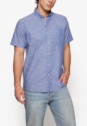 Camisa de manga corta con botones en tela azul claro jaspeada, con un bolsillo en el pecho y cuello estándar, combinada con jeans azul claro.