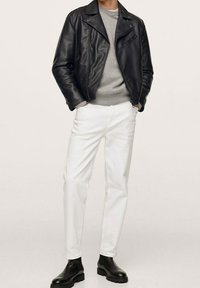 Giacca da motociclista in pelle nera, maglione grigio, jeans bianchi a gamba dritta e stivaletti neri. Texture liscia e dettagli del design aderenti.