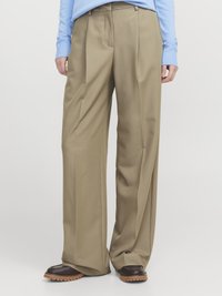 Beige weit geschnittene Hose aus einem glatten Stoff, mit Falten und hoher Taille. Kombiniert mit dunkelbraunen Schnürschuhen.