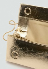 Guldmetal taske med en struktureret overflade, udstyret med en kædedesign, to runde metaløjer og en beige indvendig foring.