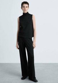 Schwarzes ärmelloses Turtleneck-Oberteil, kombiniert mit weiten schwarzen Hosen. Aus strukturiertem Stoff gefertigt, mit lockerer Passform und minimalistischem Design.