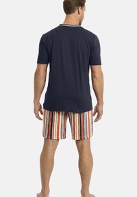 Kurzeilige Marineblau-T-Shirt kombiniert mit mehrfarbigen gestreiften Shorts mit senkrechten Linien in Orange, Weiß und Blau. Baumwollmaterial, lässiges Design.