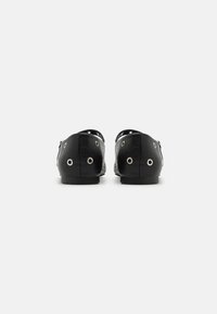 Chaussures en cuir noir au design épuré, avec des œillets ronds en métal argenté sur les côtés et une semelle plate et lisse.