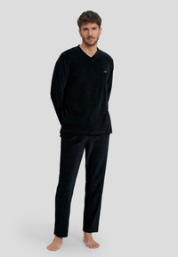 Conjunto de loungewear de terciopelo negro que incluye una camiseta de cuello en V de manga larga y pantalones a juego, con una textura suave y un corte relajado.