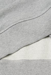 Felpa grigia con una trama a coste e un morbido rivestimento in pile bianco. Presenta un design semplice e bordi cuciti, con il tessuto stratificato visibile.