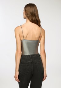 Metaliczny srebrny body z cienkimi spaghetti ramiączkami, zestawione z wysokim stanem ciemnoszarymi dżinsami z tylnymi kieszeniami i gładką teksturą.