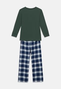 Hosszú ujjú sötétzöld felső kék-fehér kockás flanel nadrággal párosítva. Az anyag puhanak tűnik, kényelmes, laza szabással.