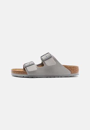 Graue Sandalen mit zwei verstellbaren Riemen, Korkfußbett und strukturierter Gummisohle, die über eine glatte Oberfläche und eine abgerundete Zehenform verfügen.