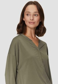 Olivgrüne Bluse mit langen Ärmeln, V-Ausschnitt und lässiger Passform. Weicher Stoff und minimale Nähte für ein entspanntes Erscheinungsbild.